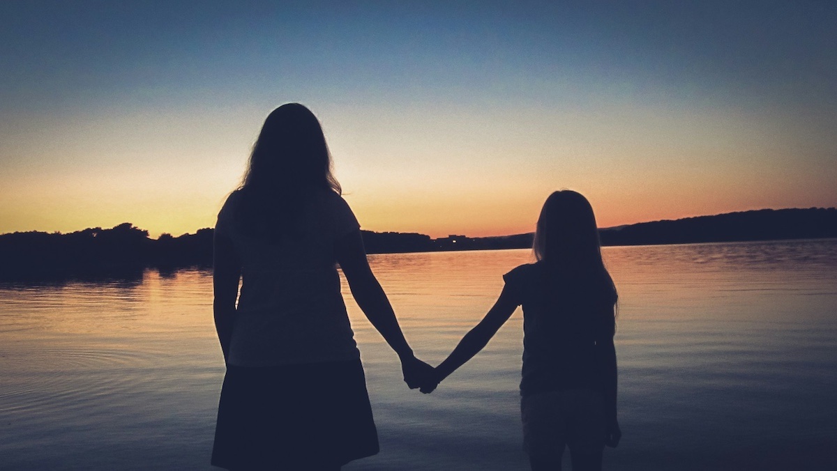 Silhouette di madre e figlia sulla spiaggia al tramonto, simbolo di amore, libertà e connessione profonda.