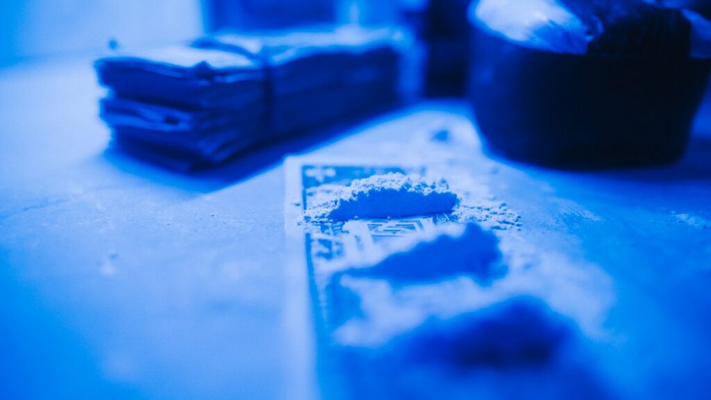 Immagine ravvicinata di banconote arrotolate accanto a polvere bianca su un tavolo, simbolo del consumo di sostanze stimolanti