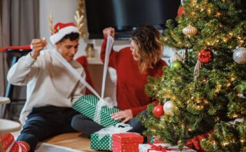 Uomo e donna che aprono pacchetti regalo seduti insieme, con espressioni gioiose e intime