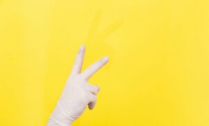 Mano che fa il segno di pace con guanto blu, immagine simbolica legata a sicurezza, consenso e massaggio prostata