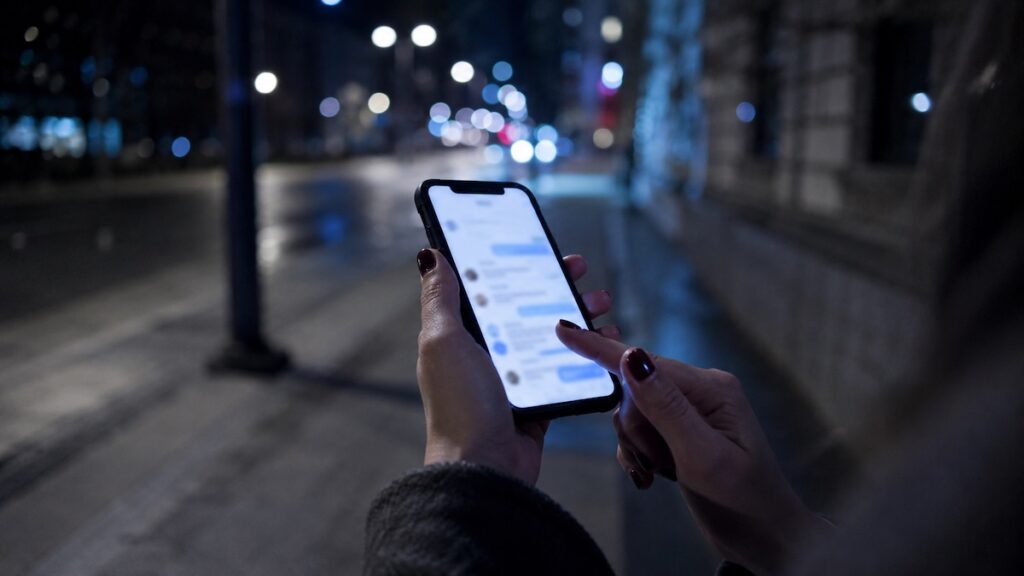 Mani femminili che tengono uno smartphone durante la notte in città