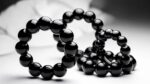 Anelli penieni in silicone nero lucido a sfere su tessuto bianco morbido, still life elegante