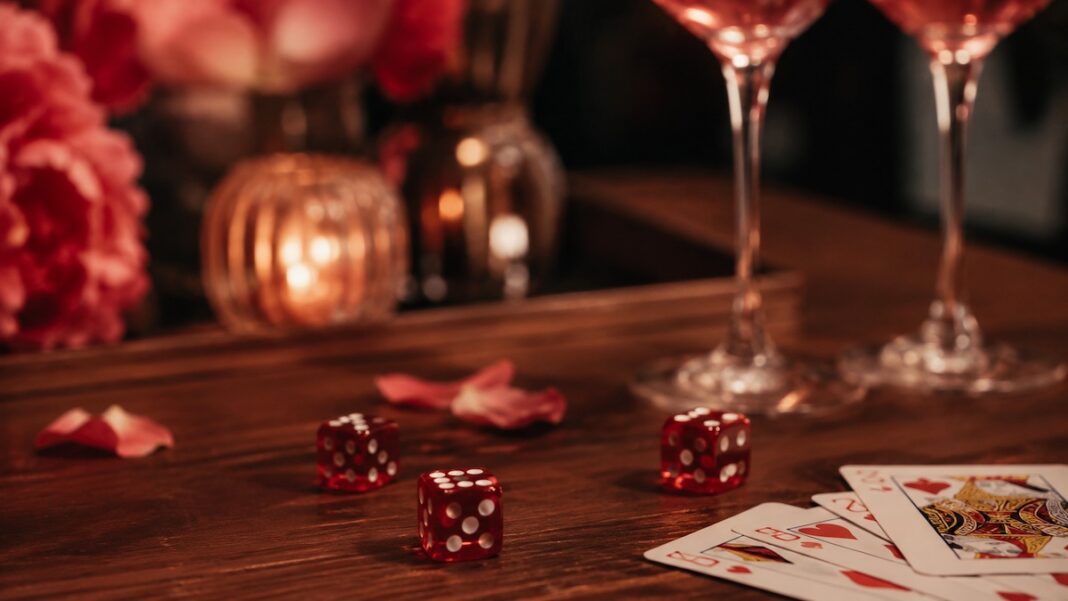 Dadi e carte su un tavolo con luce calda e due calici sullo sfondo, immagine sui giochi erotici per donne e di coppia