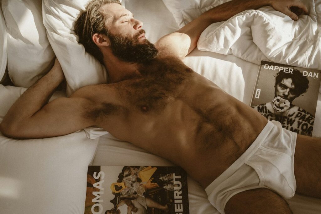Uomo a torso nudo disteso sul letto in un contesto intimo e riflessivo.