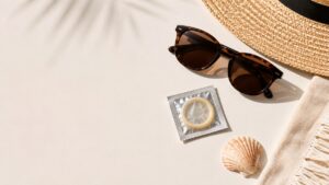 Preservativo accanto a occhiali da sole e oggetti estivi, immagine sulla prevenzione delle infezioni sessualmente trasmissibili in estate