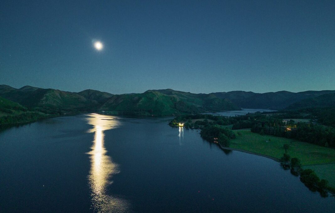 Luna piena che si riflette su un lago circondato dalle montagne